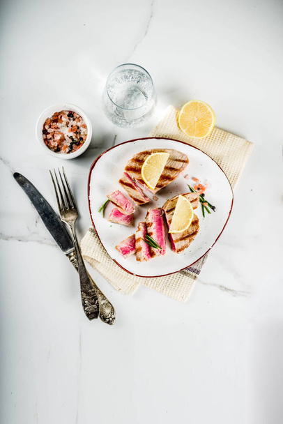 Grilled tuna fish steaks with lemon and spices, on portioned plate, white marble background copy space top view - Fotó, kép