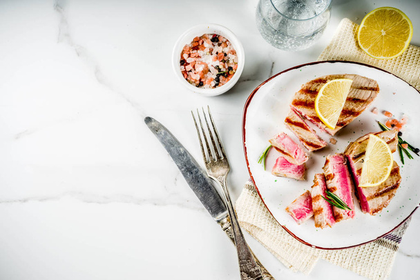 Steaks de thon grillés au citron et aux épices, sur une assiette en portions, blanc marbre fond copie espace vue du dessus
 - Photo, image