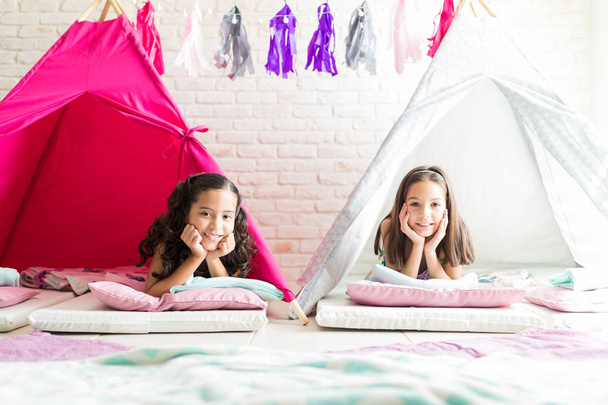 Portrait de filles détendues avec les mains sur le menton souriant dans des tentes de tipi à la maison
 - Photo, image