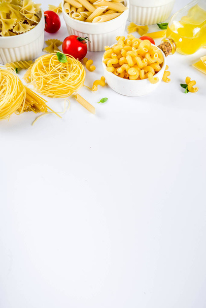 Ιταλικό φαγητό έννοια, ποικιλία διάφορα ωμά ζυμαρικά - μακαρόνια, λαζάνια, βίδες, ταλιατέλες, Πέννες, τορτελίνια, ραβιόλια, με ντομάτες και βασιλικό φύλλα λευκό φόντο αντίγραφο χώρου κάτοψη - Φωτογραφία, εικόνα
