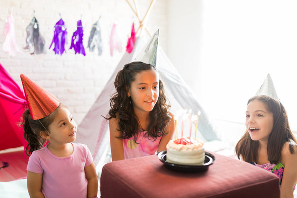 Mädchen singt Geburtstagslied für Freundin beim Kuchenschauen während Schlummerparty zu Hause - Foto, Bild