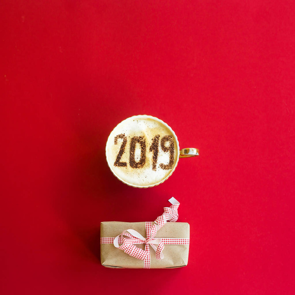 Das neue Jahr 2019 steht auf einer Tasse Kaffee mit Milch. das Konzept des neuen Jahres am 1. Januar auf rotem Hintergrund mit einem Geschenk. Draufsicht, flache Lage - Foto, Bild