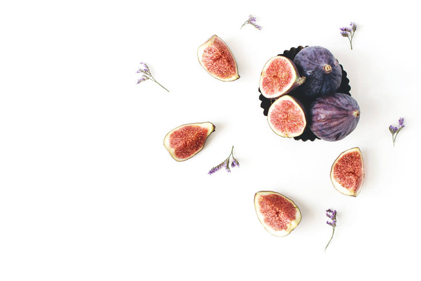 Fresh ripe purple figs composition. Food Photo. Sliced and whole exotic fruit in vintage bowl. Limonium flowers on a white table background. Floral pattern, decorative corner. Flat lay, top view. - 写真・画像