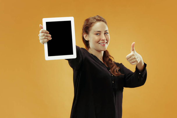 Portrait of a confident casual girl showing blank screen of laptop isolated over studio background - Foto, imagen