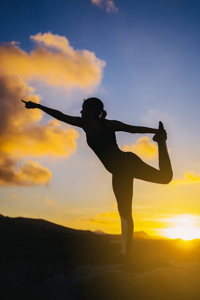 sylwetka młoda kobieta praktykowania jogi na plaży o zachodzie słońca. - Zdjęcie, obraz