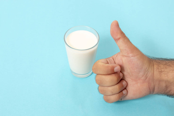 hand gives thumbs up for glass of milk on a blue background. - Fotoğraf, Görsel