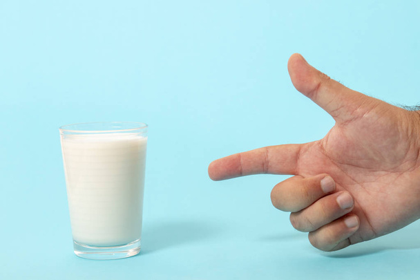finger pointing to glass of milk on a blue background. - Fotoğraf, Görsel