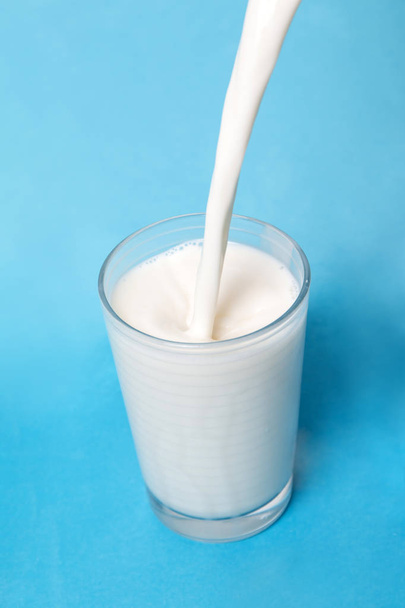 Milch auf Glas auf blauem Hintergrund gießen. - Foto, Bild