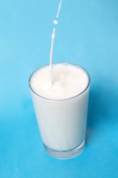 pouring milk on glass isolated on a blue background. - Foto, imagen