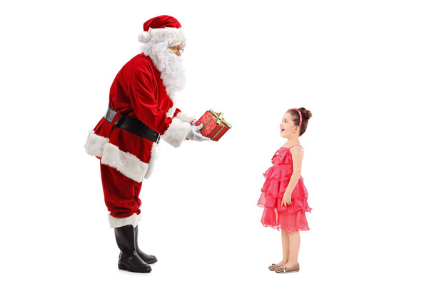 Full length profile shot of Santa Claus giving a present to a happy little girl isolated on white background  - Fotó, kép