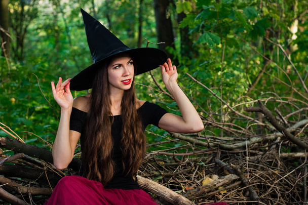Hintergrund ist der Halloween-Feiertag. Halloween-Hexe in einem dunklen Wald. schöne junge Frau mit Hexenhut und Kostüm. - Foto, Bild