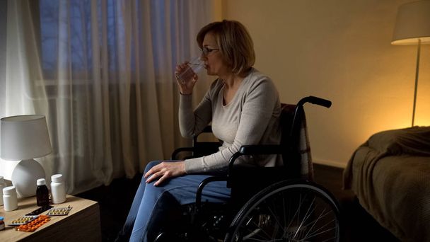 Senior lady in wheelchair taking prescribed pills rehabilitation at nursing home - 写真・画像
