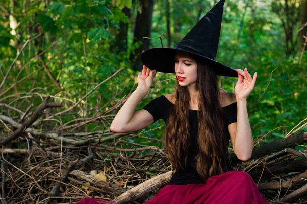 Tło wakacje Halloween. Halloween czarownica w ciemnym lesie. Piękna młoda kobieta w strój i kapelusz czarownic. - Zdjęcie, obraz