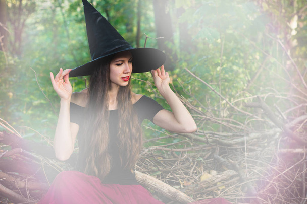 Fondo de vacaciones de Halloween. Bruja de Halloween en un bosque oscuro con efecto tonificado. Hermosa joven con sombrero de brujas y traje
. - Foto, imagen