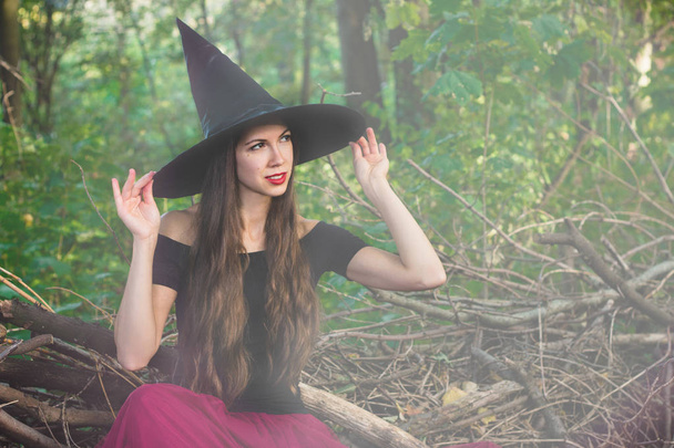 Halloween holiday background. Halloween Witch in a dark forest with toned effect. Beautiful young woman in witches hat and costume. - Photo, Image