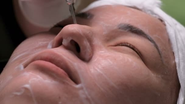 Close-up of asian female face on galvanic cleaning of the skin. Girl on the therapeutic procedure of disincrustation in the beauty salon. The work of a beautician with an electrical apparatus. - Footage, Video