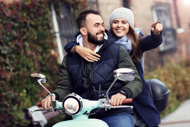 Picture of beautiful young couple smiling while riding scooter in city in autumn - Photo, Image