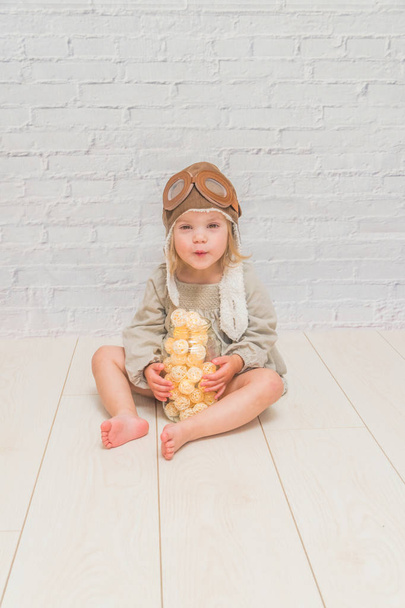a  girl, kid sitting on the floor with a garland in a jar in a pilot's helmet - Foto, afbeelding