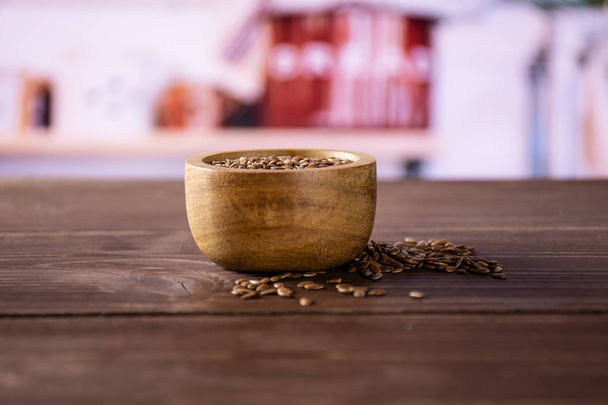 Lot of whole fresh brown flaxseeds with wooden bowl with grey kitchen in background - Foto, afbeelding