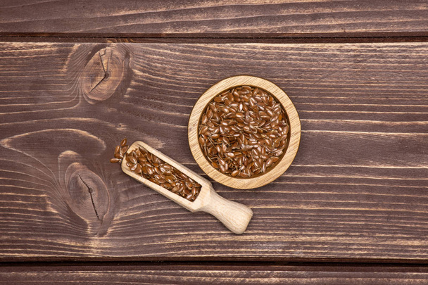 Lot of whole fresh brown flaxseeds in a scoop with wooden bowl flatlay on brown wood - Foto, Imagem