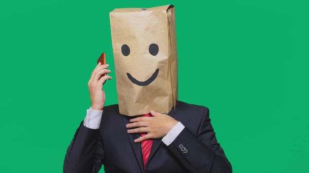 koncepcja emocje, gesty. człowiek z torby papierowe na głowie, malowane emotikon, uśmiech, radość. rozmowy na telefon komórkowy - Zdjęcie, obraz