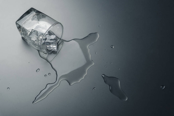 крупним планом склянку води з кубиками льоду, що розливаються на столі
 - Фото, зображення