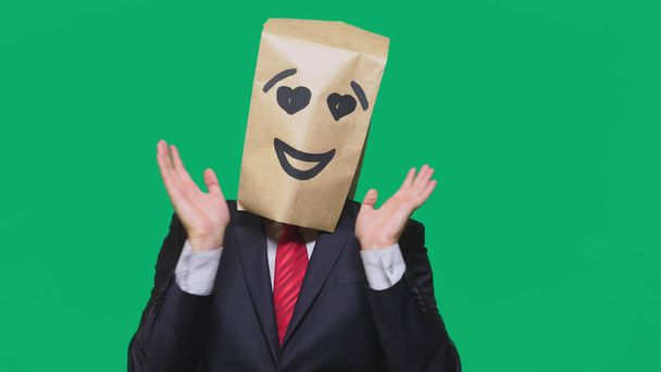 Konzept der Emotionen, Gesten. ein Mann mit Papiertüten auf dem Kopf, mit einem aufgemalten Emoticon, Lächeln, Freude, Liebesaugen. - Foto, Bild