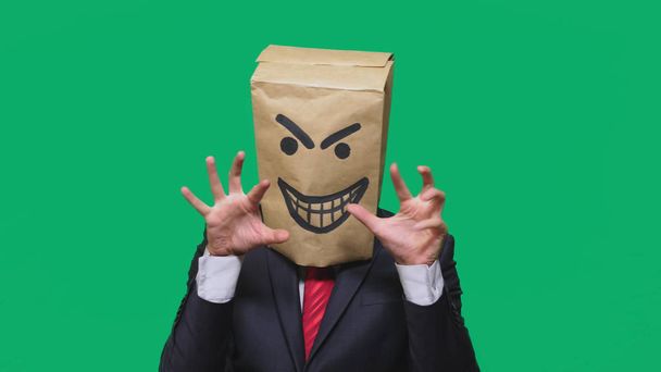 Konzept der Emotion, Gesten. ein Mann mit einem Paket auf dem Kopf, mit einem aufgemalten Smiley wütend, listig, schwelgend - Foto, Bild