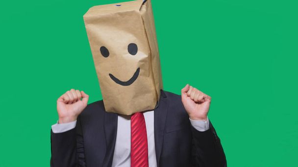 concept van emoties, gebaren. een man met papieren zakken op zijn hoofd, met een geschilderde emoticon, glimlach, vreugde - Foto, afbeelding