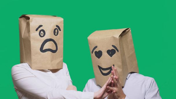 concept of emotions, gestures. a couple of people with bags on their heads, with a painted emoticon, a smile, eyes in love, and the second with a mask of fright, fear. sexual harassment concept - Photo, Image