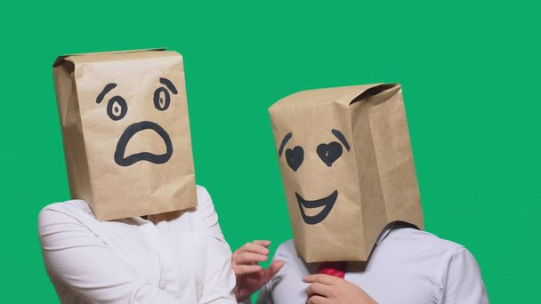 concept of emotions, gestures. a couple of people with bags on their heads, with a painted emoticon, a smile, eyes in love, and the second with a mask of fright, fear. sexual harassment concept - Photo, Image