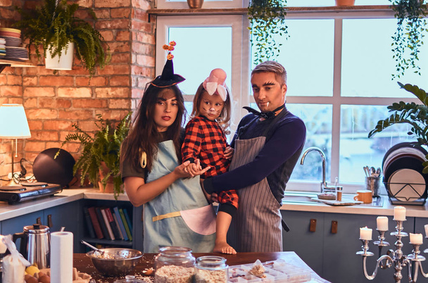 Mamma papà e figlioletta con trucco e cappelli che cucinano insieme in cucina in stile loft al mattino
. - Foto, immagini