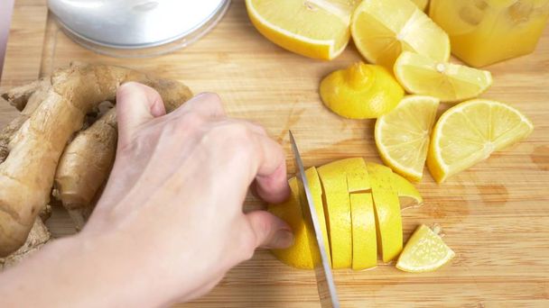 female hands cut a knife with lemon for a drink made from citrus handmade with ginger root - Foto, immagini