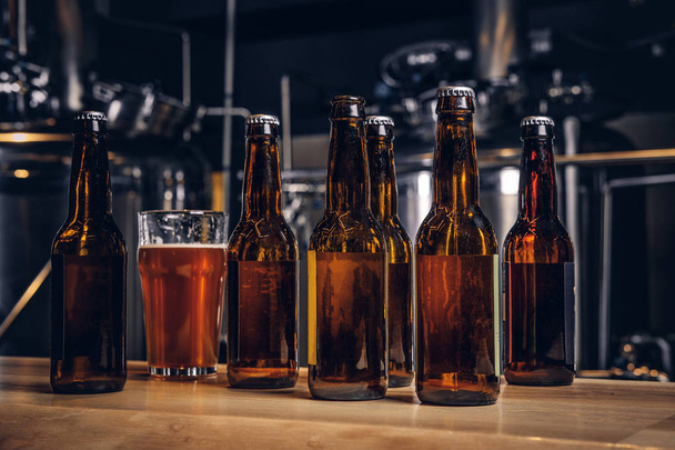 Bottles and glass of craft beer on wooden bar counter at the indie brewery. - Foto, Imagem