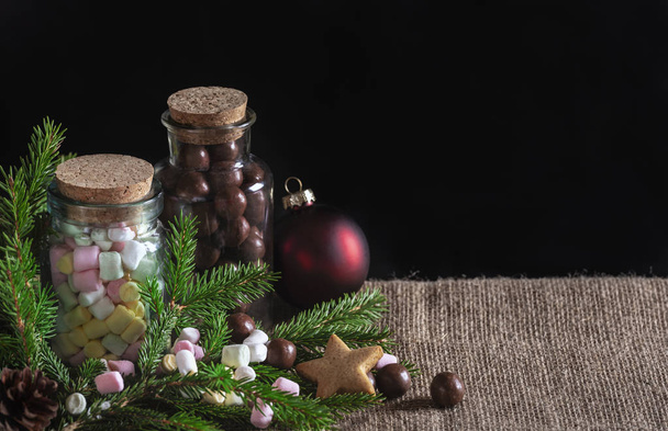 Boże Narodzenie traktuje banner z butelki pełen wielokolorowych mini marshmallows i cukierki czekoladowe, jodły zielone gałązki i Xmas piłki, na tkaniny jutowe. - Zdjęcie, obraz