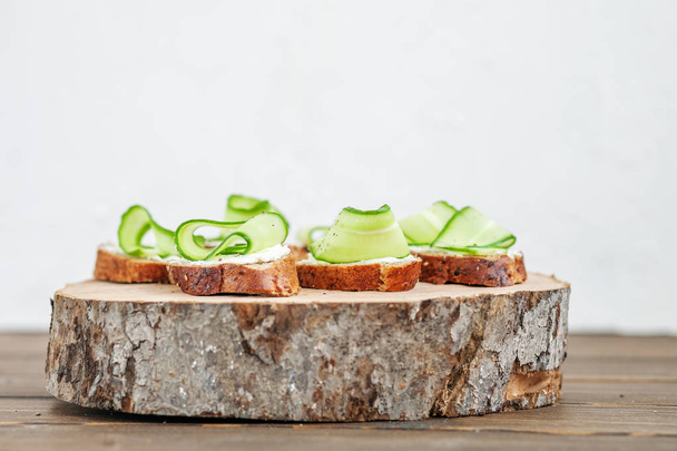 Snacks con queso feta y pepino en una tabla de madera. El concepto de comida y vegetarianismo
. - Foto, Imagen