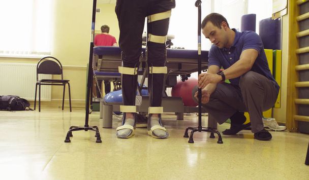 Legs of invalid in orthosis with two walking cane - Photo, Image