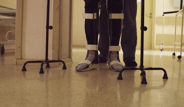 Beine von Invaliden im orthesen Gehen mit Unterstützung von zwei Gehstöcken - Foto, Bild