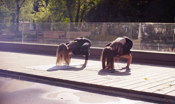 Yoga. Twee aantrekkelijke vrouw doen yoga oefeningen in het park - Foto, afbeelding