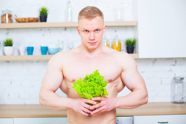 Muscular man with a naked torso in the kitchen with a salad, concept of healthy eating. Athletic way of life. - Foto, afbeelding