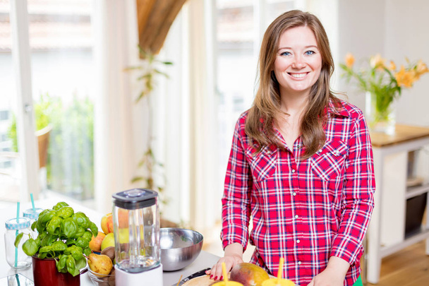Young smiling woman making smoothie with fresh greens in the blender in kitchen at home. - 写真・画像