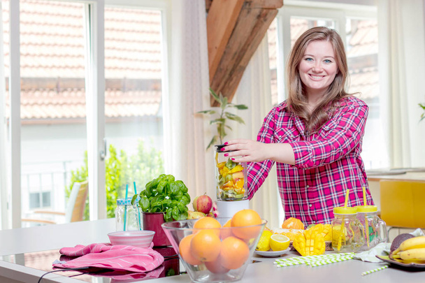 Young smiling woman making smoothie with fresh greens in the blender in kitchen at home. - Zdjęcie, obraz