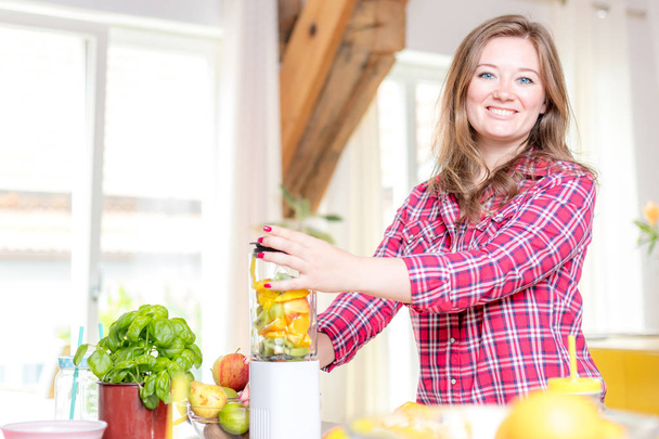 Young smiling woman making smoothie with fresh greens in the blender in kitchen at home. - Foto, Bild