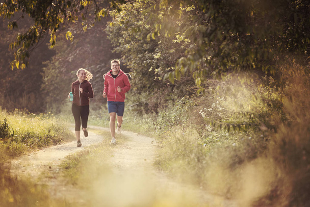 young couple enjoying healthy lifestyle while jogging along country road - Foto, Bild