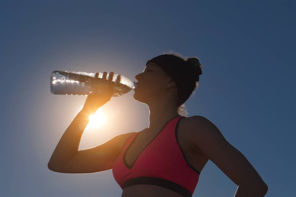 Αθλητισμός γυναίκα πόσιμο νερό από το μπουκάλι ενάντια στον ήλιο - Φωτογραφία, εικόνα