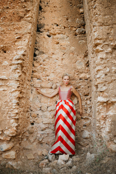 Uma bela mulher loira elegante no vestido vermelho posando perto da antiga parede de pedra do castelo. Espanha
 - Foto, Imagem