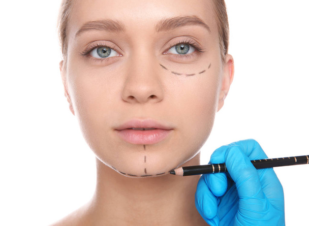 Doctor marking young woman face before cosmetic surgery on white background - Fotó, kép