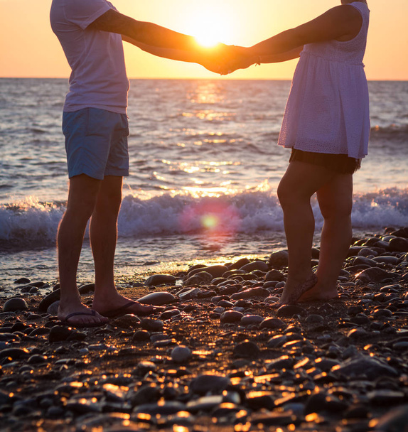 Jonge paar hand in hand op het strand bij zonsondergang - Foto, afbeelding