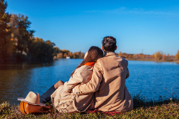 Νεαρό ζευγάρι στην αγάπη ψύξη από φθινόπωρο στη λίμνη. Ευτυχισμένος άνθρωπος και γυναίκα απολαμβάνοντας τη φύση και την αγκαλιάζει. Χαλάρωση στους εξωτερικούς χώρους - Φωτογραφία, εικόνα