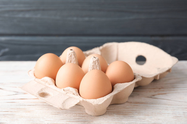 Carton of raw chicken eggs on wooden table against gray background - Foto, imagen